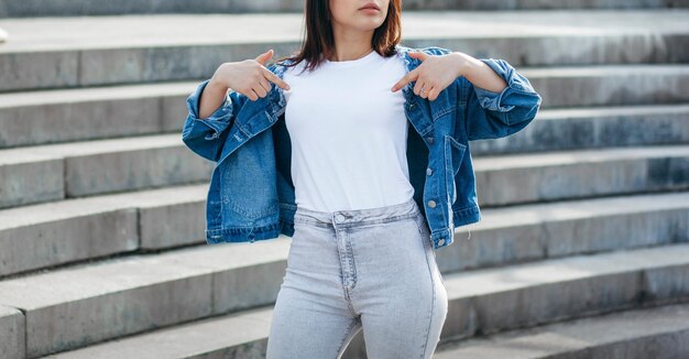 Elegante ragazza bruna che indossa una maglietta bianca e occhiali in posa contro lo stile di abbigliamento urbano di strada