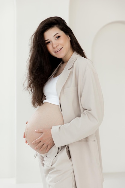 Elegante ragazza bruna incinta con tailleur pantalone beige