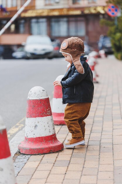Elegante ragazzo di 3 anni in giacca di pelle e pantaloni marroni cammina per strada Bambino moderno Moda per bambini Bambino felice