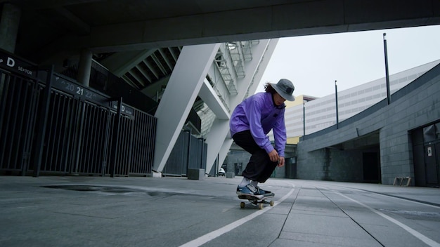 Elegante ragazzo skater che salta sullo skateboard al centro Giovane hipster che si gode gli sport estremi all'aperto Persona maschile attiva che si bilancia su skateboard all'aperto nella mattinata estiva