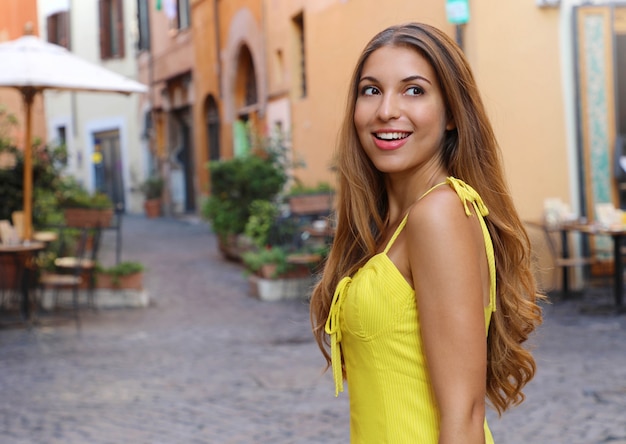 Elegante ritratto di bella moda donna con i capelli lunghi in abito estivo giallo a piedi nel quartiere di Trastevere a Roma, Italia.