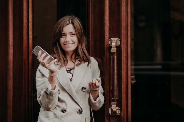 Elegante splendida signora in impermeabile, tiene il telefono cellulare, attende la chiamata