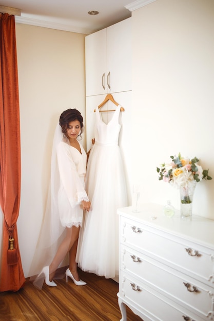Elegante sposa in abito bianco che posa sotto la tenda straordinaria sposa nella preparazione mattutina