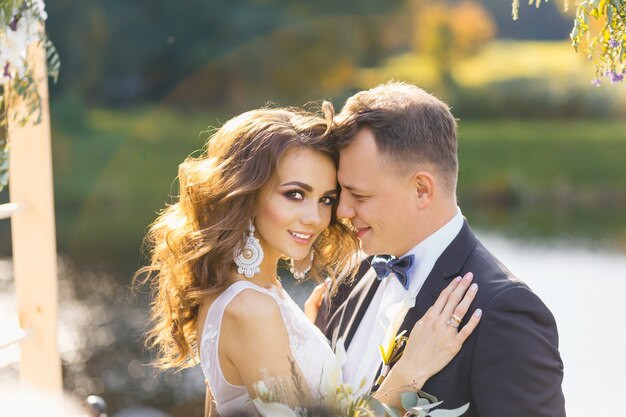 Elegante sposa riccia e sposo felice all'aperto sullo sfondo del lago. Cerimonia di matrimonio creativa ed elegante