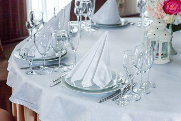 Elegante tavola apparecchiata per la cena con composizione floreale in ristorante, sfondo interno di lusso. Matrimonio elegante decorazione per banchetti e articoli per il cibo organizzati dal servizio di catering sul tavolo bianco.