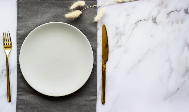 Elegante tavola con piatto grigio vuoto posate dorate su tovagliolo di lino Decorazione da tavola
