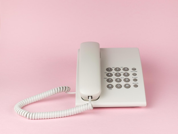 Elegante telefono da ufficio cablato bianco su sfondo rosa Piatto