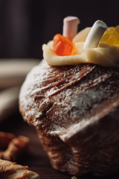 Elegante torta pasquale con marshmallow e orsetti di gelatina su uno sfondo di legno rustico scuro.