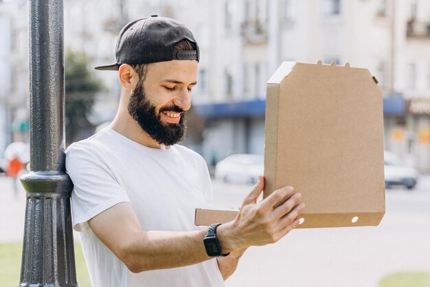 Elegante uomo barbuto con una scatola di cartone di pizza sotto il tuo testo o logo