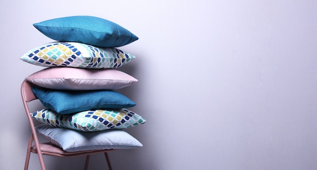 Eleganti cuscini colorati in camera sul muro grigio. Cuscini blu scuro, rosa, blu sulla sedia. Copi lo spazio, concetto domestico accogliente.