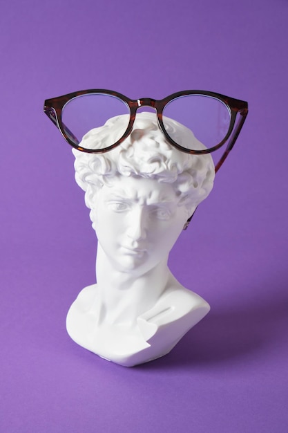 Eleganti occhiali con scultura in gesso su uno sfondo di colore viola alla moda, spazio per la copia Busto di David