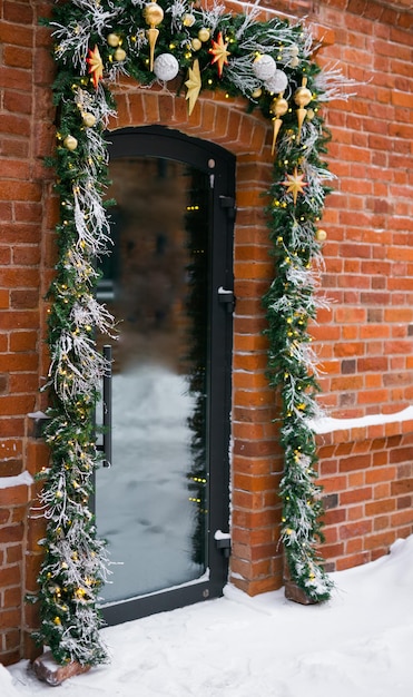 Eleganti rami di abete natalizio con palline e ghirlanda scintillante davanti alla porta al mercato delle vacanze o al ristorante in strada cittadina Decorazioni natalizie invernali