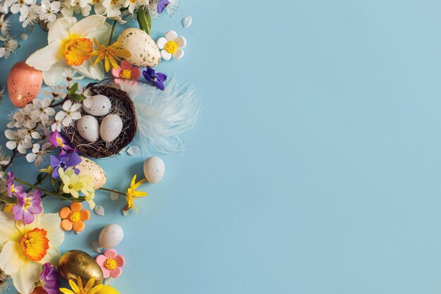 Eleganti uova di Pasqua nel nido fiori colorati e fiori di ciliegio distesi su sfondo blu con spazio di copia Modello di biglietto di auguri di buona Pasqua Banner di vacanza moderna Composizione festiva