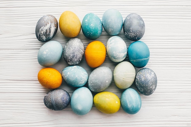 Eleganti uova di pasqua su fondo di legno bianco piatto lay Uova di pasqua moderne dipinte con colorante naturale in colore marmo giallo grigio blu Biglietto d'auguri con motivo di Pasqua felice