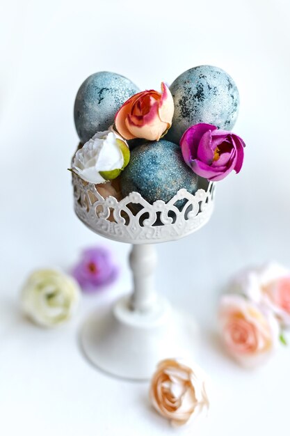 Eleganti uova dipinte di blu in un vaso vintage con fiori decorativi in tessuto. Bellissimo tavolo floreale per auguri di buona Pasqua con messa a fuoco selettiva.