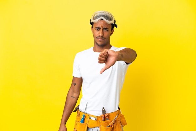 Elettricista afroamericano sopra il muro giallo isolato che mostra il pollice verso il basso con espressione negativa
