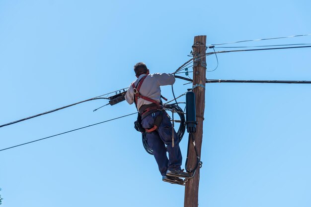 Elettricista maschio che fissa i cavi della città in alto sopra la città sulla scala con cablaggio