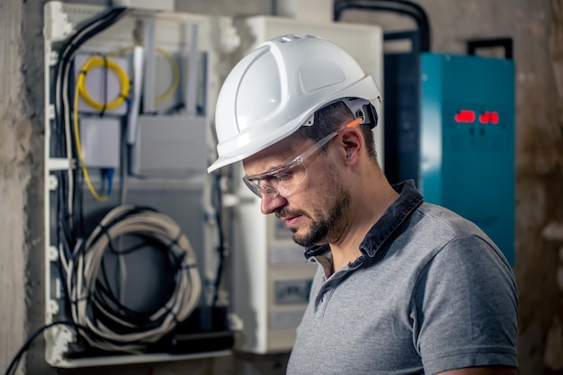 Elettricista maschio con occhiali di sicurezza e casco vicino al quadro elettrico