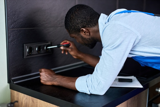 Elettricista sicuro, ripara, installa la presa in cucina. Maestro dell'uomo nella presa di torsione complessiva con cacciavite funzionante, riparando. maschio che lavora alla spina elettrica sull'impianto elettrico residenziale