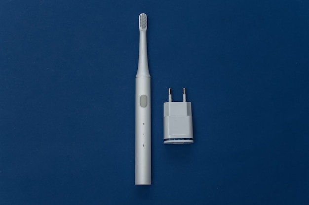 Elettro-spazzolino con caricatore su sfondo blu classico. Colore 2020. Vista dall'alto