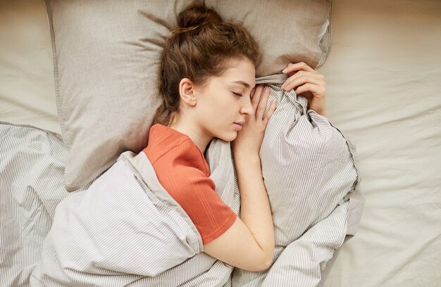 Elevato angolo di visione della giovane donna sdraiata sul cuscino con gli occhi chiusi che dorme con una coperta nel letto