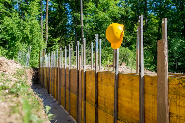 Elmetto protettivo giallo appeso a pannelli di legno supportati su un cantiere in un concetto di costruzione e costruzione, all'aperto in un'area boschiva.