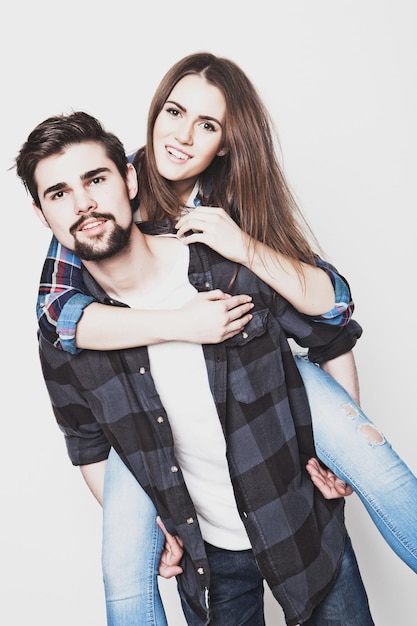 Emotivo stile di vita felicità e concetto di persone Felice coppia amorosa Giovane uomo sulle spalle della sua ragazza Studio girato su sfondo bianco Foto tonificanti alla moda speciali