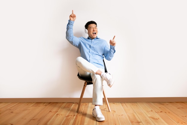 Emotivo uomo d'affari asiatico di mezza età che utilizza cuffie wireless per ascoltare musica e ballare