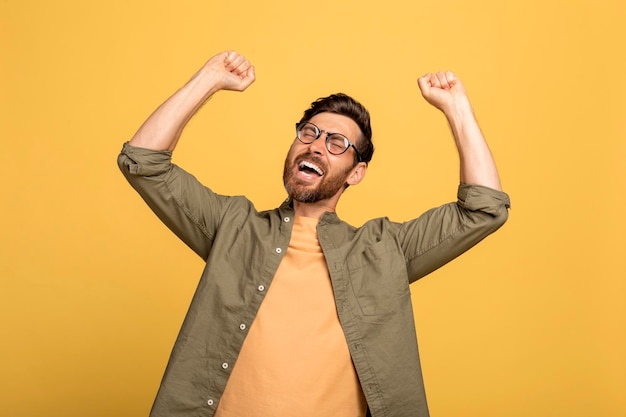 Emozionale felice uomo di mezza età esclamando e stringendo i pugni festeggiando il successo sullo studio giallo