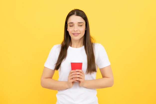 Emozione di giovane bella donna bere caffè caldo bellezza viso trucco naturale isolato su sfondo giallo