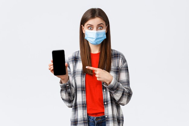 Emozioni diverse, covid-19, distanza sociale e concetto di tecnologia. Donna interessata ed eccitata in maschera medica che punta lo schermo del telefono cellulare con il dito, promuove l'app o ordina sul sito di shopping.