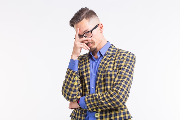 Emozioni e concetto di persone - bel giovane in giacca con barba e baffi in bicchieri pensando a qualcosa sopra il muro bianco.