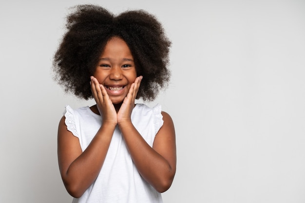 Emozioni felici del bambino sorpreso. Ritratto di una bambina adorabile che si tiene per mano sul viso e sorride con stupore, tenendo la bocca spalancata, espressione scioccata. Studio girato isolato su sfondo bianco