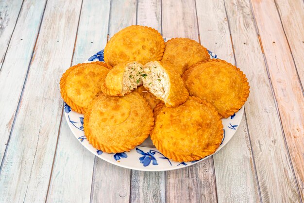 Empanadas ripiene di carne di pollo tirata con prezzemolo su piatto bianco e fiori blu