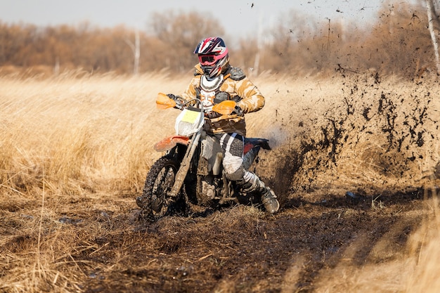 Enduro bike rider in un campo con erba secca in autunno. La moto sbanda e fa molti schizzi di fango