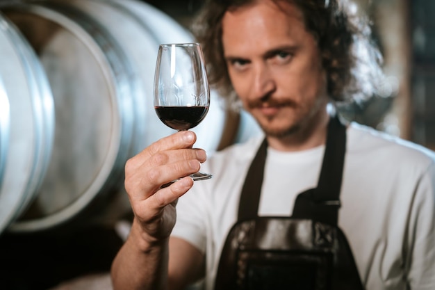 Enologo che degusta vino in una cantina con botti di legno