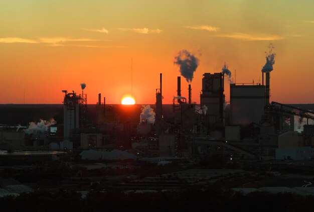 Enorme fabbrica con camini alti che inquinano l'atmosfera con fumo di anidride carbonica dal processo di produzione presso il cantiere di produzione dell'impianto Sito industriale al tramonto