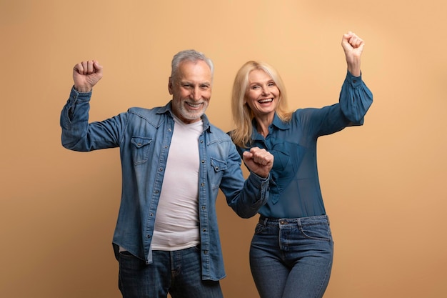 Entusiasta coppia di pensionati felice che celebra il successo su sfondo beige