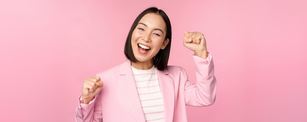 Entusiasta donna d'affari asiatica aziendale alzando la mano e tifo trionfando vincendo e celebrando in piedi su sfondo rosa