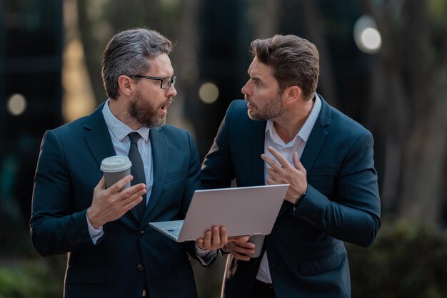 Entusiasti sorpresi due team di uomini d'affari che utilizzano il team di uomini d'affari all'aperto del computer portatile del tablet che lavorano o