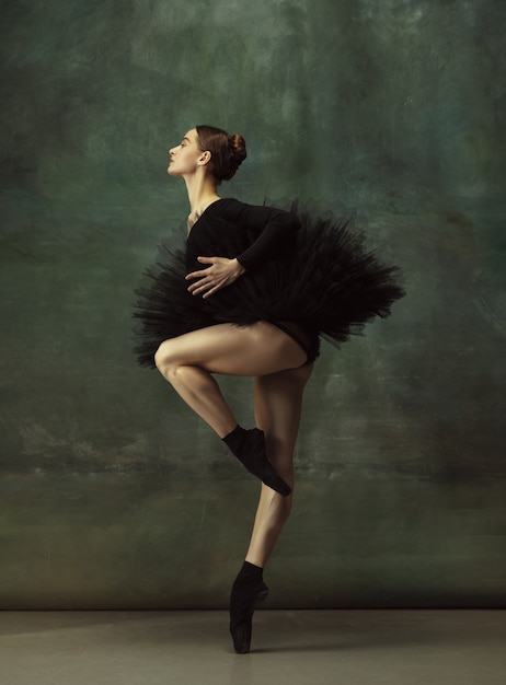 Equilibrato. Graziosa ballerina classica che balla, posa isolata su sfondo scuro studio. Tutù nero di eleganza. Grazia, movimento, azione e concetto di movimento. Sembra senza peso, flessibile. Alla moda.