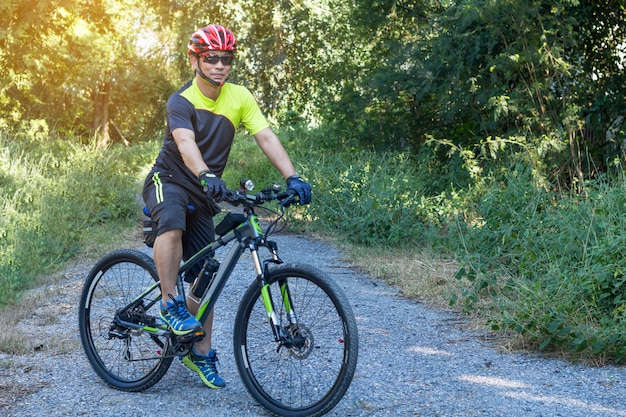 Equipaggi con il guanto del casco per sicurezza che guida una bicicletta alla strada della campagna lungo una foresta