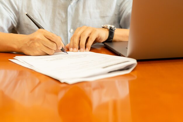 Equipaggi i documenti di firma con la penna e il computer portatile di spoletta sullo scrittorio di legno.