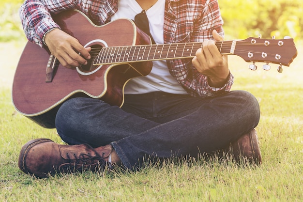 Equipaggi il gioco della chitarra, sedentesi sull&#39;erba verde