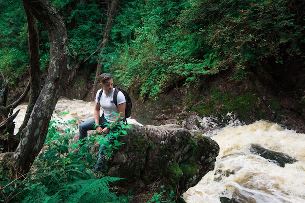 Equipaggi il viaggiatore con lo zaino che si siede sulla roccia nella foresta