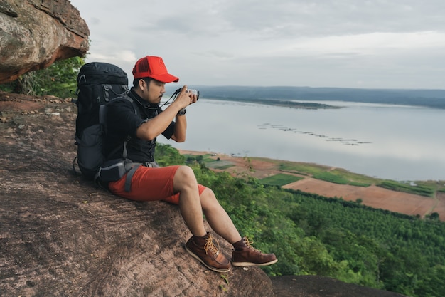 Equipaggi il viaggiatore con lo zaino facendo uso della macchina fotografica che prende una foto sul bordo della scogliera, su una cima della montagna della roccia