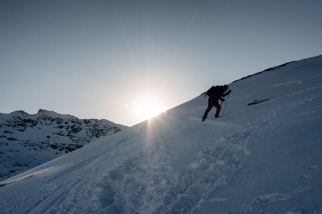 Equipaggi l'alpinista che scala sulla montagna nevosa nell'inverno al tramonto