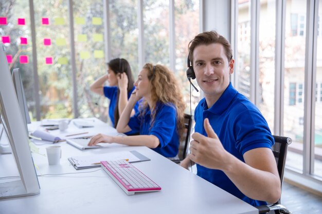 Equipaggi l'operatore che si siede i pollici su ad uno scrittorio davanti al computer