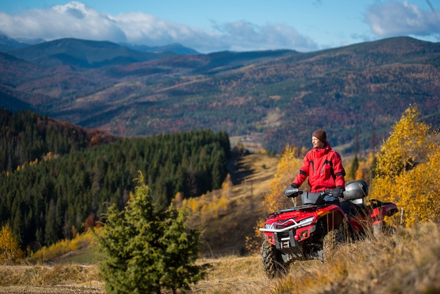 Equipaggi la guida su un ATV rosso sulle strade della montagna un giorno soleggiato di autunno