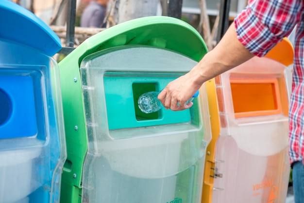 Equipaggi la mano che tiene e che mette lo spreco di plastica della bottiglia nei rifiuti dell&#39;immondizia.